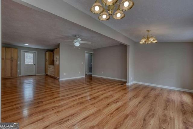 unfurnished living room featuring visible vents, ceiling fan with notable chandelier, a textured ceiling, light wood-style floors, and baseboards