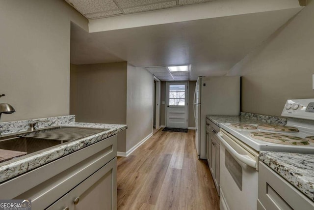 kitchen with white appliances, baseboards, light wood-style flooring, a drop ceiling, and a sink
