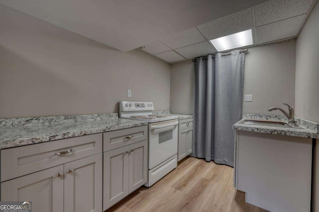kitchen featuring light stone counters, electric range, a drop ceiling, a sink, and light wood-type flooring