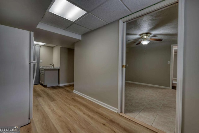 hallway featuring a sink, baseboards, a paneled ceiling, and light wood-type flooring