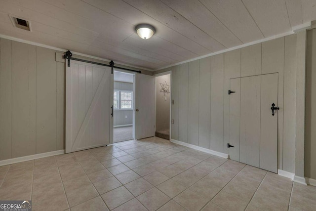 empty room with light tile patterned floors, visible vents, a barn door, and ornamental molding