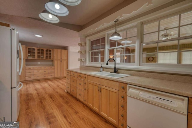 kitchen featuring light wood finished floors, light brown cabinetry, light countertops, white appliances, and a sink