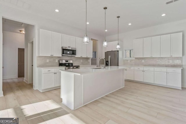 kitchen with a center island with sink, a sink, stainless steel appliances, light countertops, and white cabinetry