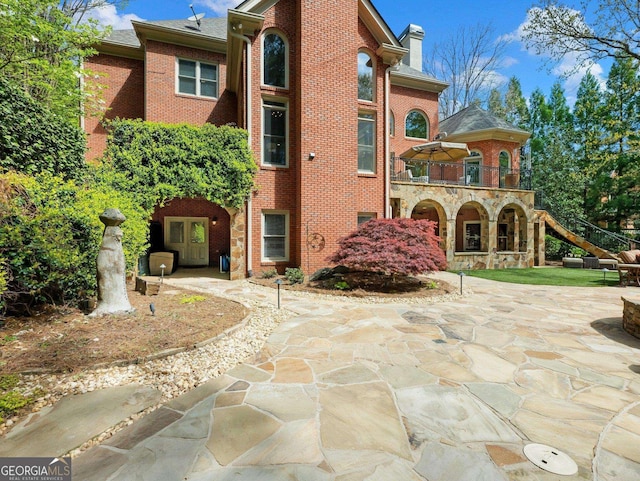 back of house with brick siding, a patio area, a chimney, and a balcony