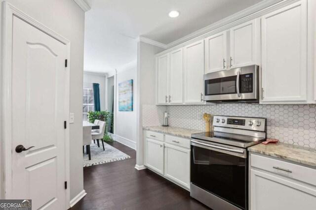 kitchen with dark wood finished floors, stainless steel appliances, white cabinetry, crown molding, and backsplash