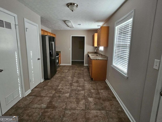 kitchen featuring visible vents, baseboards, a sink, black fridge with ice dispenser, and a textured ceiling