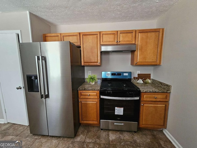 kitchen featuring under cabinet range hood, dark stone counters, appliances with stainless steel finishes, and brown cabinetry