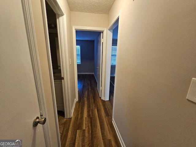 corridor with baseboards, a textured ceiling, and dark wood finished floors