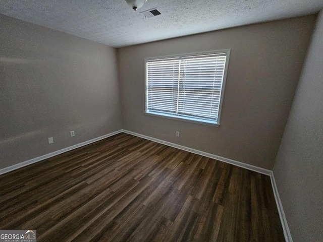 unfurnished room featuring dark wood-style floors, visible vents, a textured ceiling, and baseboards