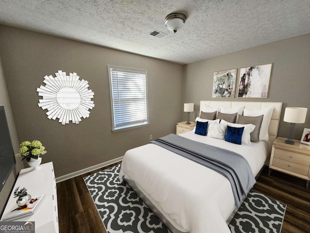 bedroom featuring dark wood finished floors, baseboards, visible vents, and a textured ceiling