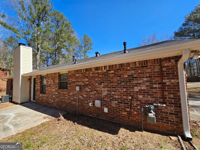 view of property exterior featuring brick siding, central AC, a chimney, and a patio