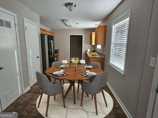 dining area featuring visible vents, baseboards, a textured ceiling, and dark tile patterned floors