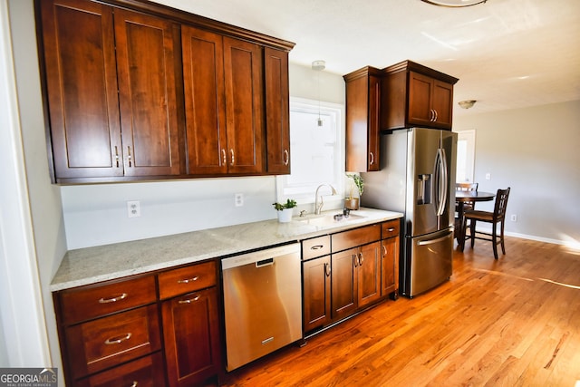 kitchen with baseboards, light stone countertops, light wood-style floors, stainless steel appliances, and a sink