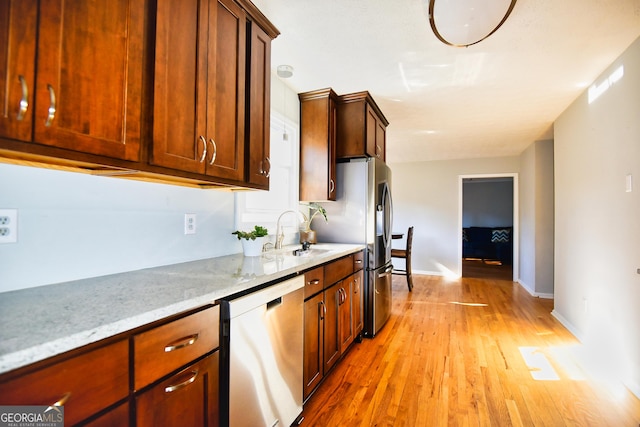 kitchen with a sink, light stone counters, light wood finished floors, baseboards, and dishwasher