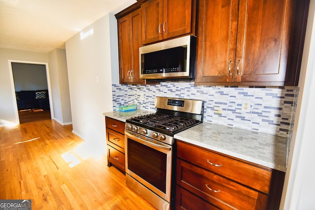 kitchen with light stone counters, baseboards, light wood-style flooring, appliances with stainless steel finishes, and tasteful backsplash