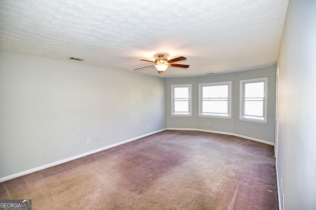 carpeted empty room with a textured ceiling, a ceiling fan, visible vents, and baseboards