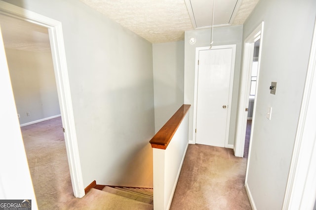 hallway featuring baseboards, attic access, an upstairs landing, carpet flooring, and a textured ceiling