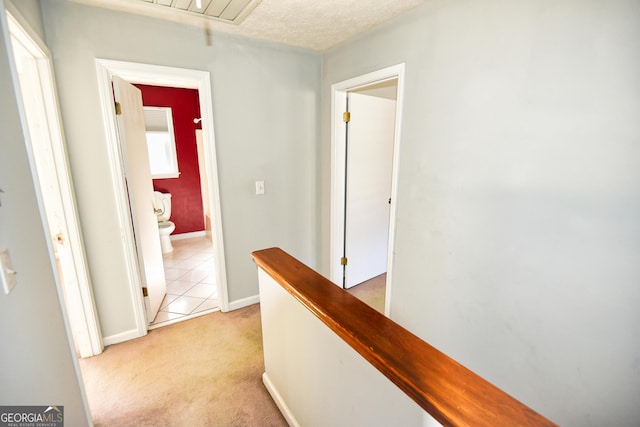 hallway featuring an upstairs landing, a textured ceiling, baseboards, light colored carpet, and attic access