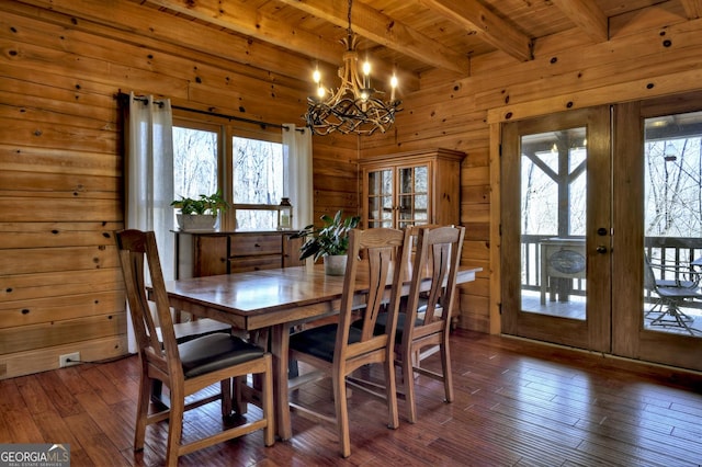 dining area with an inviting chandelier, dark wood-type flooring, wooden walls, and french doors