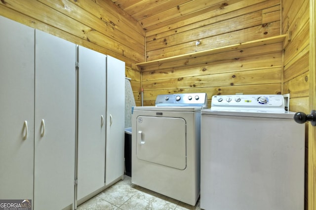 clothes washing area featuring wooden walls, cabinet space, and independent washer and dryer