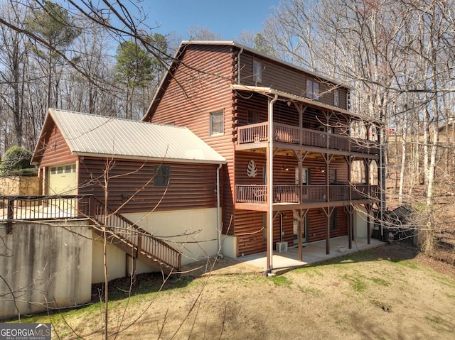 back of property with stairway, log siding, a yard, a garage, and a patio area