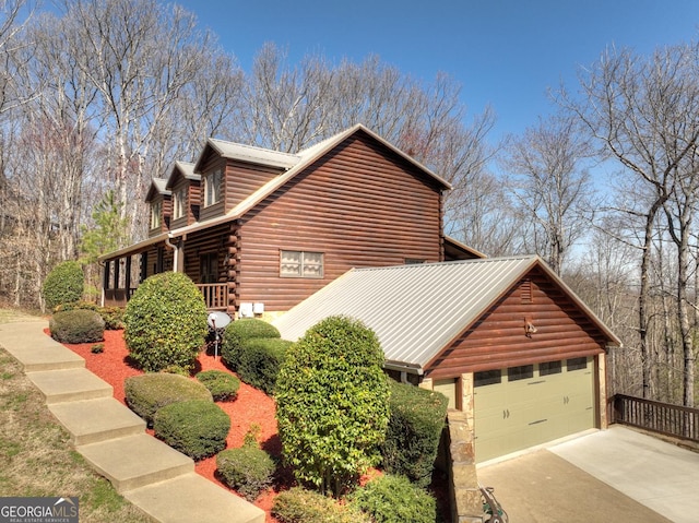 view of side of property with log exterior, an attached garage, and concrete driveway