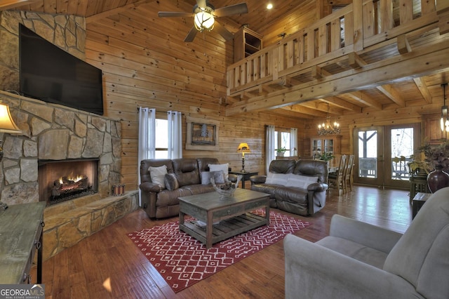 living room with wood-type flooring, a stone fireplace, wood walls, and ceiling fan with notable chandelier