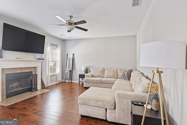 living area with visible vents, dark wood-type flooring, baseboards, ceiling fan, and a tile fireplace