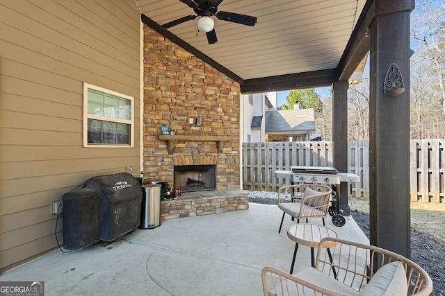 view of patio featuring area for grilling, an outdoor stone fireplace, a ceiling fan, and fence