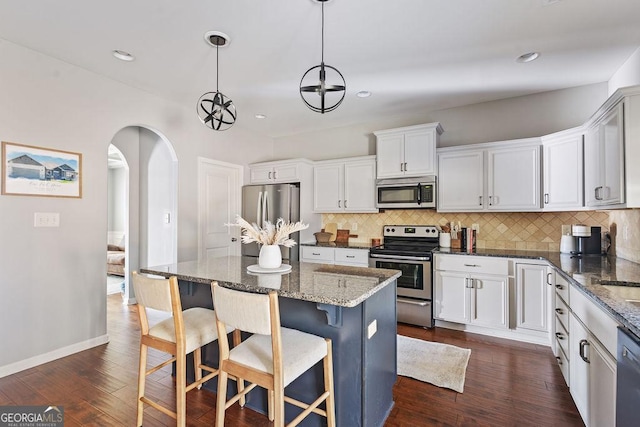 kitchen featuring white cabinetry, arched walkways, appliances with stainless steel finishes, decorative backsplash, and dark wood-style flooring