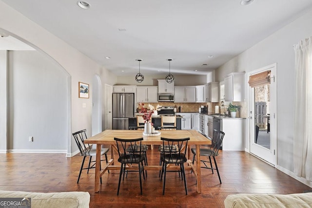 dining space featuring recessed lighting, baseboards, arched walkways, and dark wood-style flooring