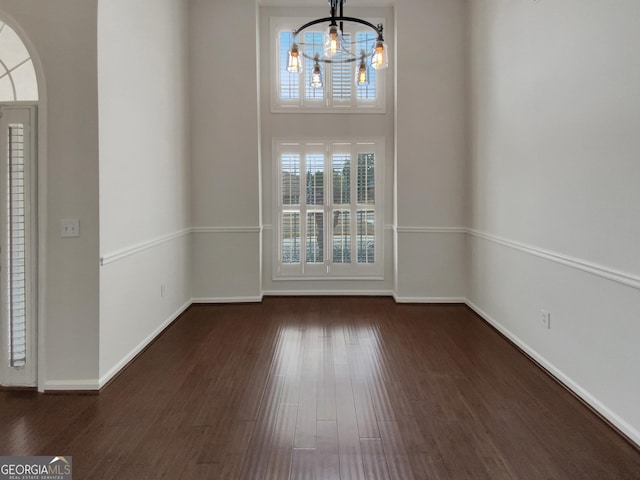 unfurnished dining area with baseboards, an inviting chandelier, and dark wood-style floors