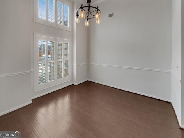 empty room featuring dark wood finished floors, a notable chandelier, baseboards, and visible vents