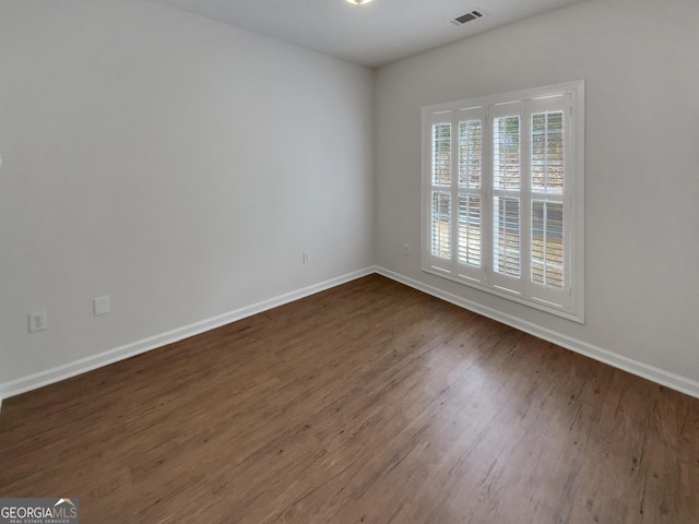 empty room featuring visible vents, dark wood-type flooring, and baseboards