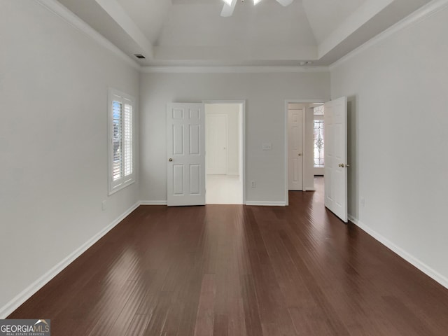 unfurnished bedroom with multiple windows, a raised ceiling, baseboards, and dark wood-style flooring