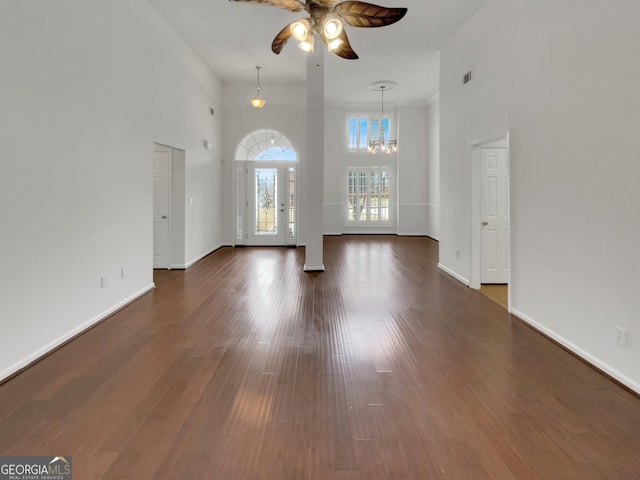 unfurnished living room with dark wood-type flooring, a high ceiling, ceiling fan with notable chandelier, and baseboards