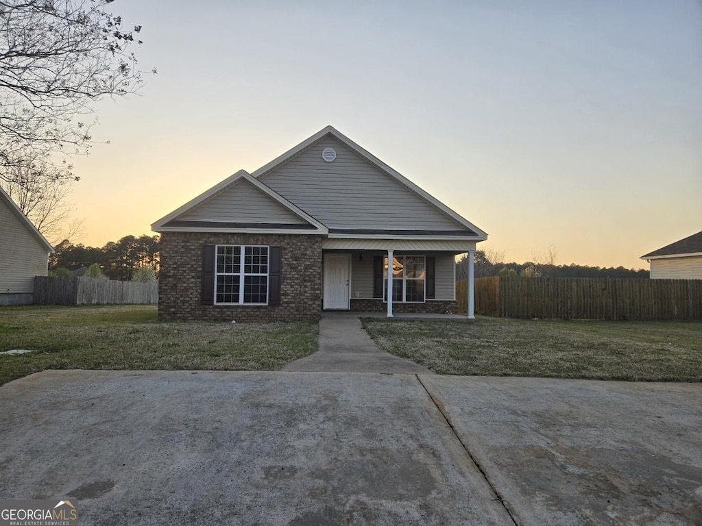 view of front of home with brick siding, covered porch, a front lawn, and fence