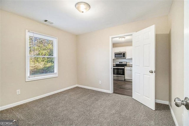 empty room with baseboards, visible vents, and dark carpet