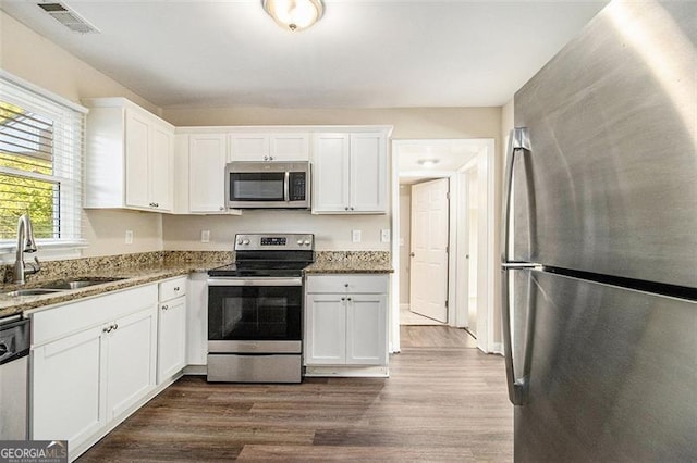 kitchen with a sink, stone countertops, dark wood finished floors, stainless steel appliances, and white cabinets