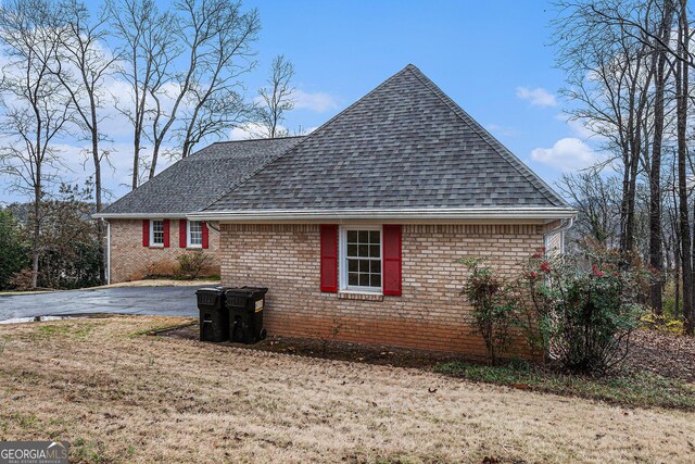view of property exterior featuring brick siding, a lawn, and a shingled roof