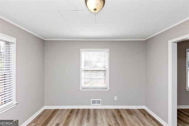 empty room with visible vents, crown molding, baseboards, and wood finished floors