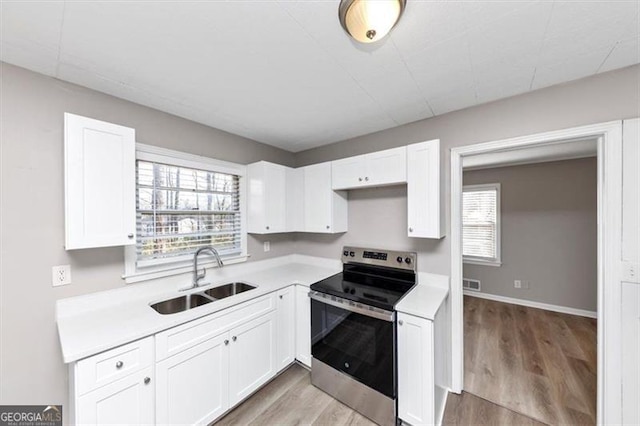 kitchen featuring light countertops, light wood-style floors, electric range, white cabinetry, and a sink