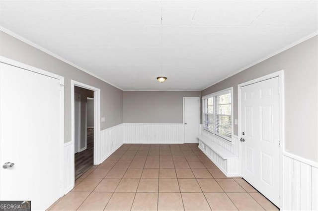 empty room featuring light tile patterned floors, a wainscoted wall, and ornamental molding