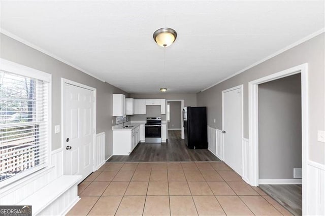 kitchen with light countertops, light tile patterned floors, freestanding refrigerator, electric range, and white cabinetry