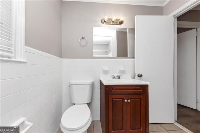 half bathroom with vanity, a wainscoted wall, tile patterned flooring, tile walls, and toilet