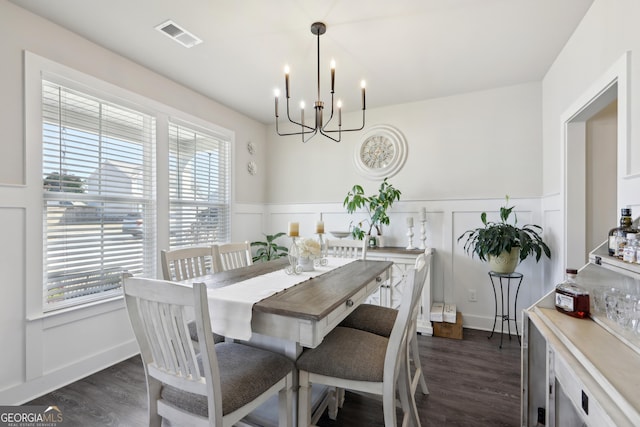 dining space featuring visible vents, dark wood finished floors, a wainscoted wall, an inviting chandelier, and a decorative wall