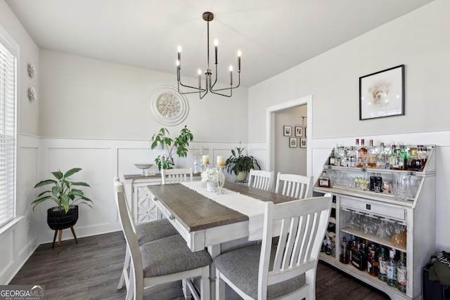 dining space featuring wood finished floors, a bar, wainscoting, a decorative wall, and a chandelier