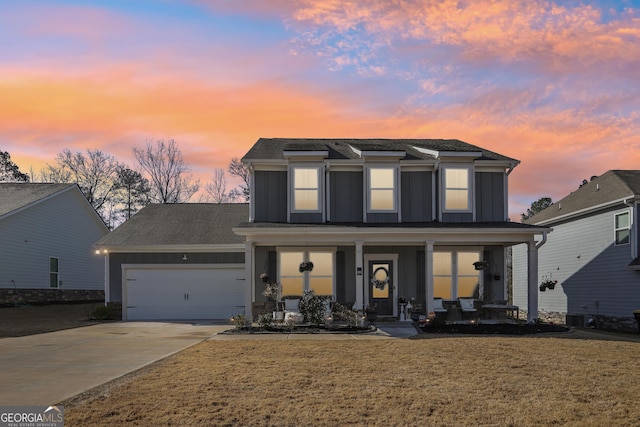 traditional home with a front yard, an attached garage, covered porch, concrete driveway, and board and batten siding