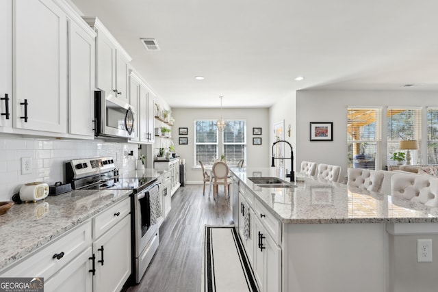 kitchen with a kitchen island with sink, a sink, tasteful backsplash, appliances with stainless steel finishes, and white cabinets