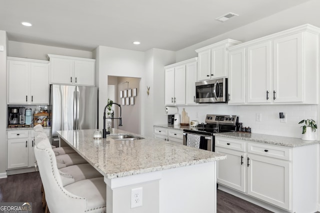 kitchen with light stone countertops, a center island with sink, a sink, stainless steel appliances, and backsplash